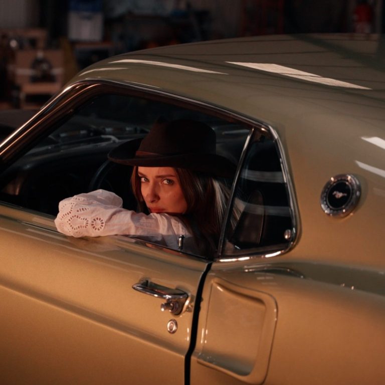 Femme dans une voiture vintage, regardant par la fenêtre avec un chapeau.