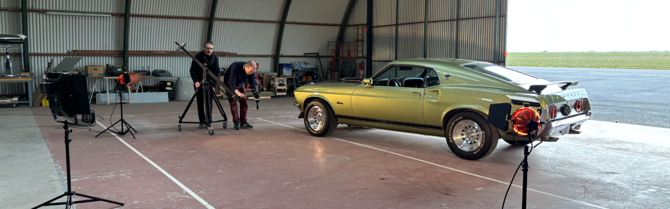 Voiture de sport verte en cours de captation dans un hangar. Équipements de tournage présents.
