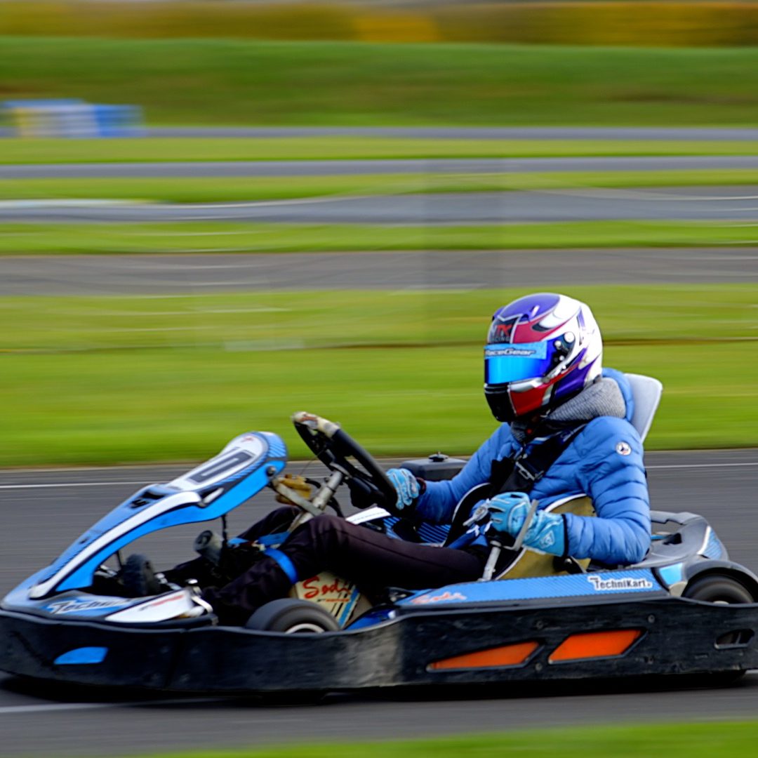 Pilote de karting en action sur une piste, portant un casque et une combinaison de course.