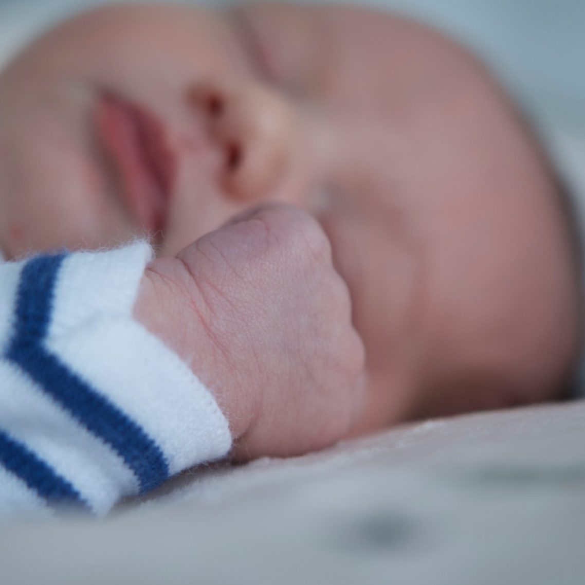 Bébé endormi avec un petit poing serré, portant un vêtement à rayures bleues.